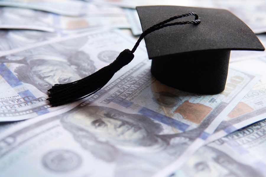 Graduation cap on top of a pile of US hundred dollar bills. Education financing, student loan concept.